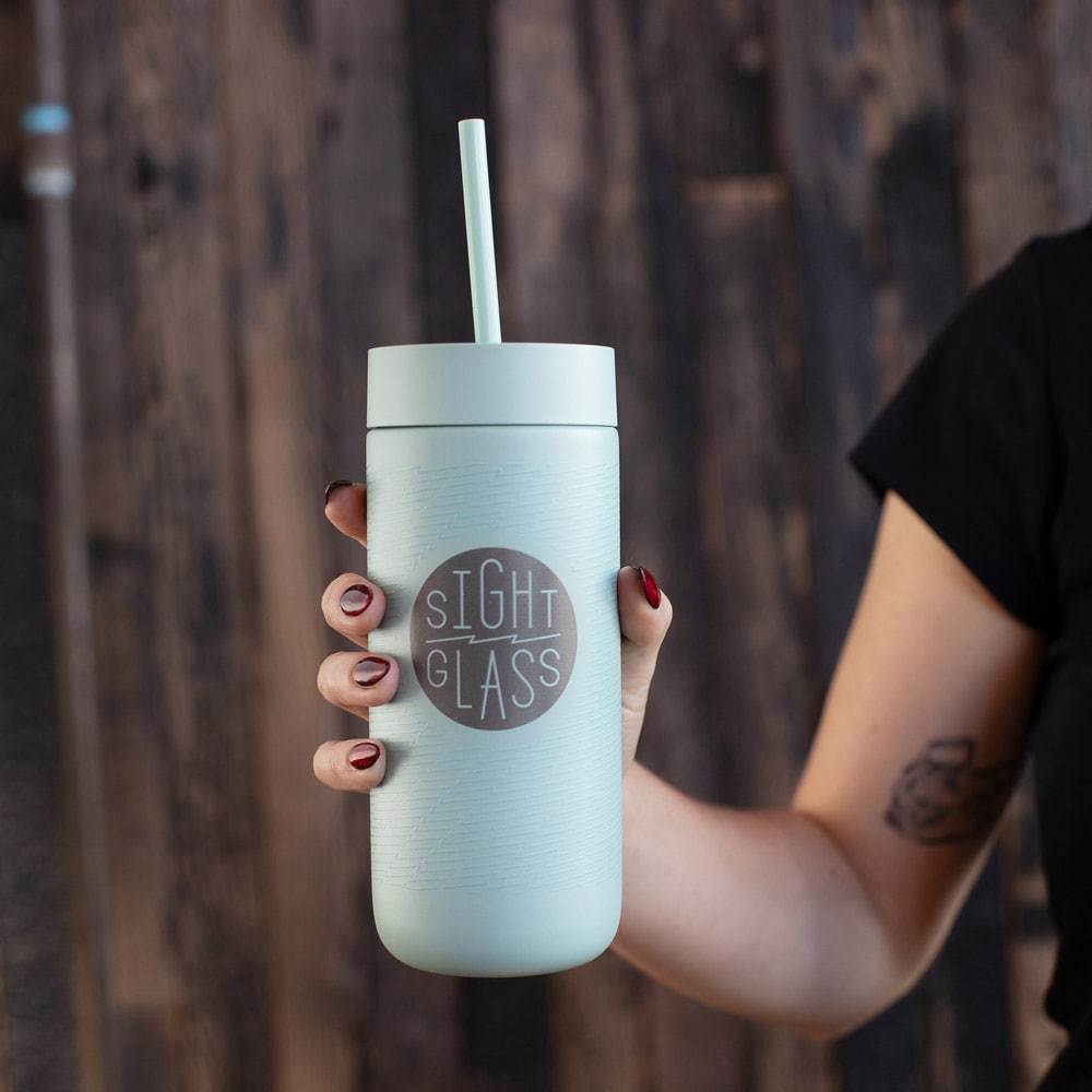 Light blue tumbler with straw held by a person against a wooden background